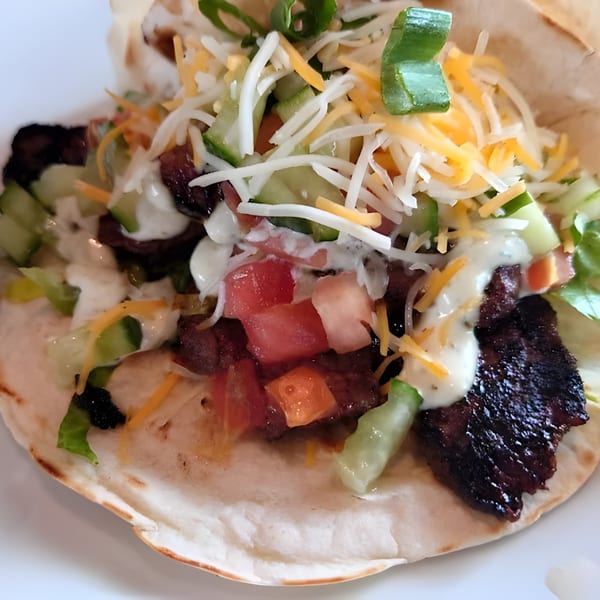 Close-up of a Liberty Tavern taco with grilled meat, shredded cheese, diced tomatoes, and sauce.