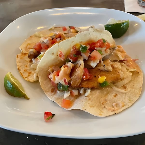 Two fish tacos with pico de gallo, sauce, and lime wedges on a white plate at Liberty Tavern.