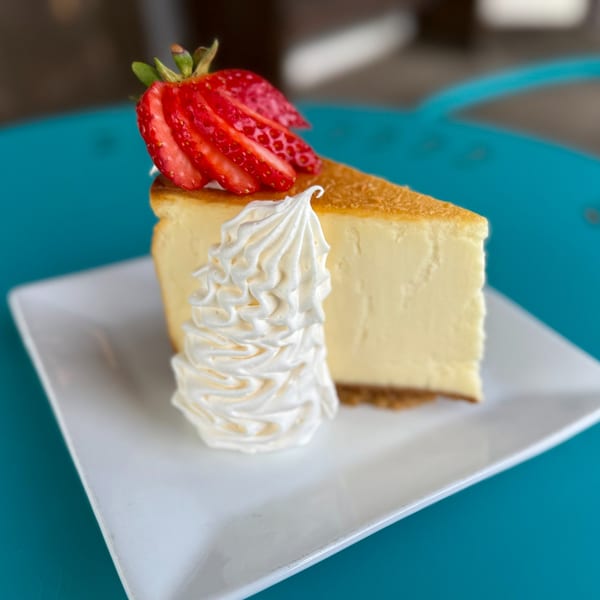 A slice of cheesecake with whipped cream and sliced strawberries on a white plate.