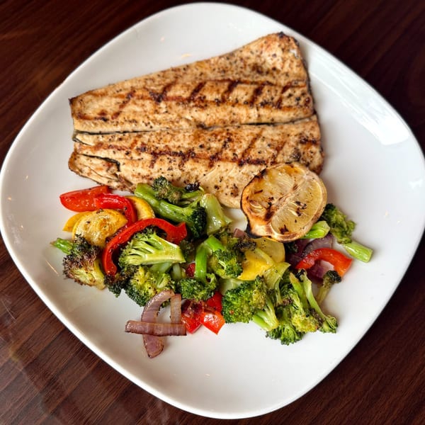 Grilled fish with char marks, roasted broccoli, red peppers, yellow squash, and a lemon wedge.