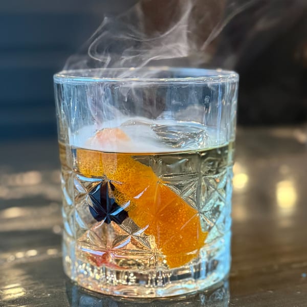 Steaming cocktail in a cut glass with an orange peel and dark cherry at Liberty Tavern.