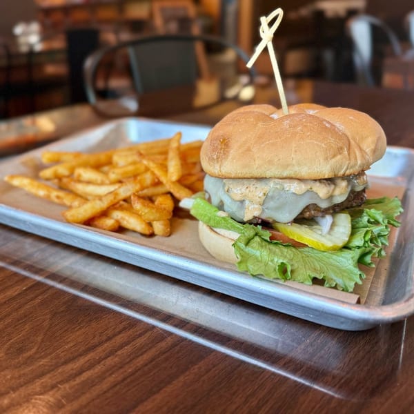 A Liberty Tavern burger with melted cheese, lettuce, tomato, pickles, and fries on a metal tray.