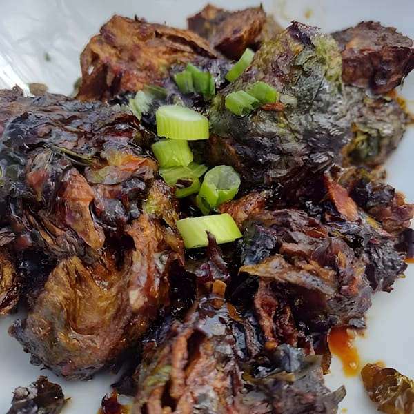 Crispy, dark Brussels sprouts with a glossy sauce and fresh green onions on a white plate.
